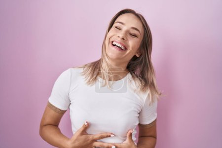 Téléchargez les photos : Blonde caucasian woman standing over pink background smiling and laughing hard out loud because funny crazy joke with hands on body. - en image libre de droit