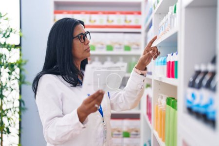 Téléchargez les photos : Middle age hispanic woman pharmacist reading prescription at pharmacy - en image libre de droit