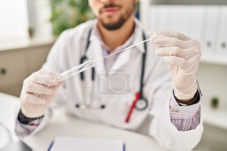Téléchargez les photos : Jeune homme arabe portant un uniforme de médecin tenant un test d'antigène à la clinique - en image libre de droit