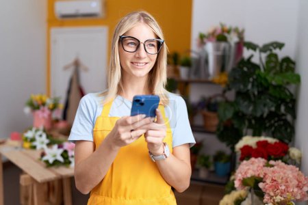 Photo for Young blonde woman florist smiling confident using smartphone at flower shop - Royalty Free Image