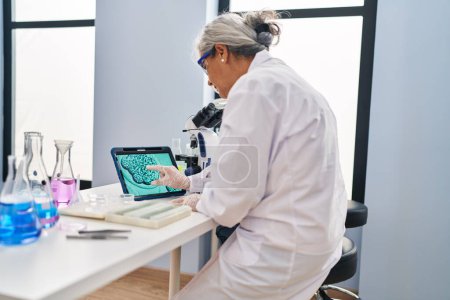 Foto de Mujer de mediana edad vistiendo uniforme científico viendo embriones en touchpad en el laboratorio - Imagen libre de derechos