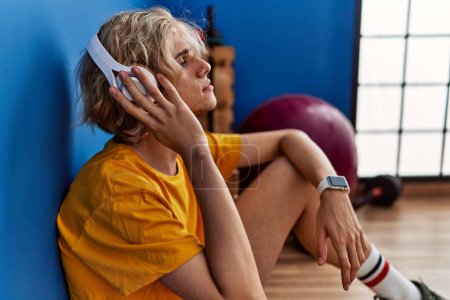 Photo for Young blond man listening to music sitting on floor at sport center - Royalty Free Image