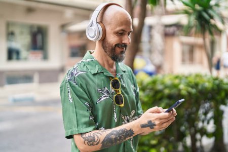 Téléchargez les photos : Jeune chauve souriant confiant écoutant de la musique dans la rue - en image libre de droit