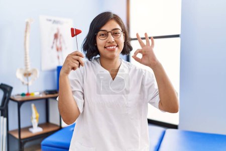 Photo for Young hispanic physiotherapist woman holding reflex hammer doing ok sign with fingers, smiling friendly gesturing excellent symbol - Royalty Free Image