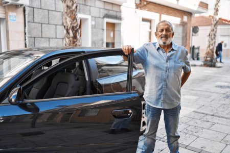 Téléchargez les photos : Homme âgé aux cheveux gris souriant confiant ouvrant la porte de la voiture dans la rue - en image libre de droit