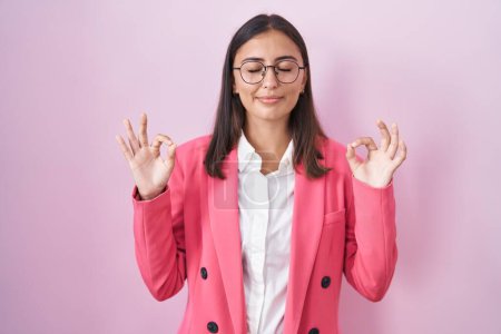 Téléchargez les photos : Young hispanic woman wearing business clothes and glasses relaxed and smiling with eyes closed doing meditation gesture with fingers. yoga concept. - en image libre de droit