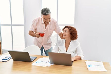 Photo for Middle age man and woman business workers drinking coffee and using laptop working at office - Royalty Free Image