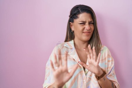 Photo for Blonde woman standing over pink background disgusted expression, displeased and fearful doing disgust face because aversion reaction. with hands raised - Royalty Free Image