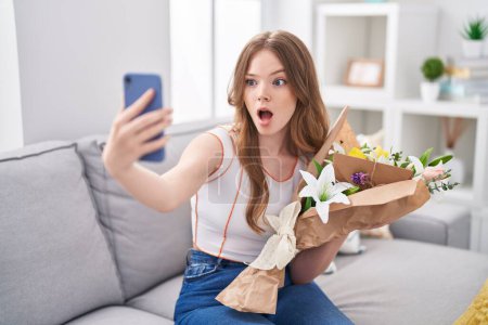 Photo for Caucasian woman holding bouquet of white flowers taking a selfie picture in shock face, looking skeptical and sarcastic, surprised with open mouth - Royalty Free Image