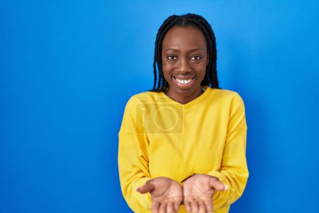 Foto de Beautiful black woman standing over blue background smiling with hands palms together receiving or giving gesture. hold and protection - Imagen libre de derechos