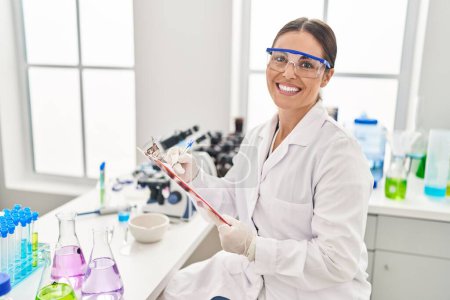Photo for Young beautiful hispanic woman scientist smiling confident writing report working at laboratory - Royalty Free Image