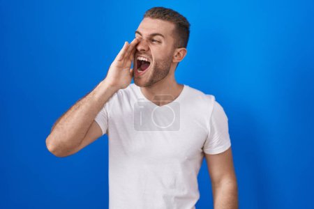 Téléchargez les photos : Young caucasian man standing over blue background shouting and screaming loud to side with hand on mouth. communication concept. - en image libre de droit