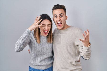 Photo for Young hispanic couple standing over white background crazy and mad shouting and yelling with aggressive expression and arms raised. frustration concept. - Royalty Free Image