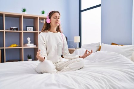 Téléchargez les photos : Young woman sitting on bed meditating at bedroom - en image libre de droit