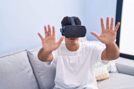 Foto de Joven hispano jugando videojuegos usando gafas de realidad virtual en casa - Imagen libre de derechos