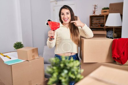 Téléchargez les photos : Young hispanic woman moving to a new home packing boxes smiling happy pointing with hand and finger - en image libre de droit