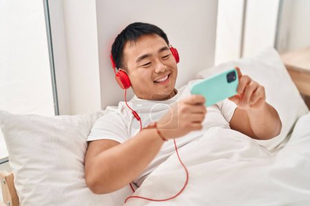 Photo for Young chinese man watching movie lying on bed at bedroom - Royalty Free Image