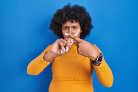 Photo for Black woman with curly hair standing over blue background rejection expression crossing fingers doing negative sign - Royalty Free Image