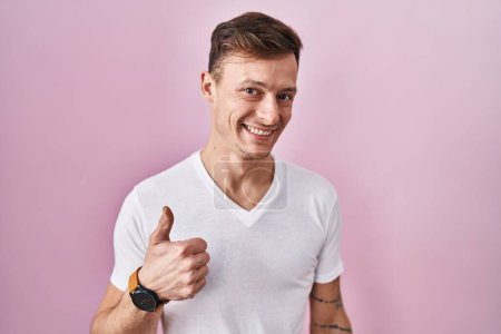 Téléchargez les photos : Caucasian man standing over pink background doing happy thumbs up gesture with hand. approving expression looking at the camera showing success. - en image libre de droit