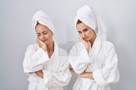 Téléchargez les photos : Femme et fille d'âge moyen portant un peignoir blanc et une serviette pensant fatigué et ennuyé par des problèmes de dépression avec les bras croisés. - en image libre de droit