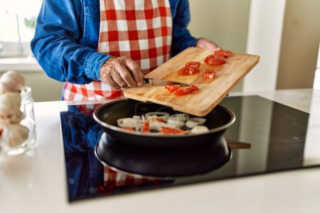 Photo for Senior man pouring tomato in frying pan at kitchen - Royalty Free Image