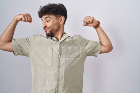 Téléchargez les photos : Arab man with beard standing over white background showing arms muscles smiling proud. fitness concept. - en image libre de droit