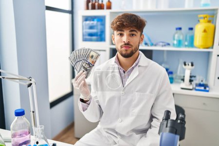 Photo for Arab man with beard working at scientist laboratory holding money thinking attitude and sober expression looking self confident - Royalty Free Image