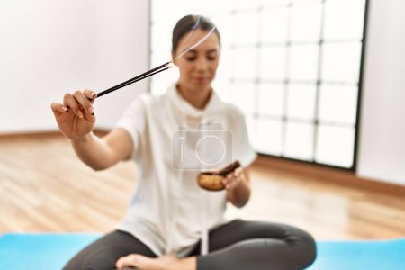 Photo for Young hispanic woman training yoga holding incense at sport center. - Royalty Free Image