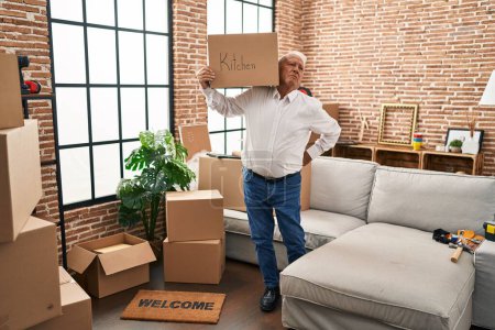 Téléchargez les photos : Homme âgé avec mal de dos tenant paquet de cuisine à la nouvelle maison - en image libre de droit