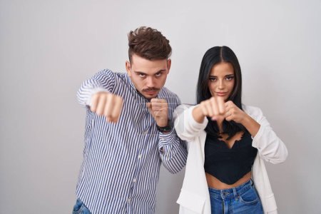 Téléchargez les photos : Jeune couple hispanique debout sur fond blanc coups de poing poing pour se battre, agressif et en colère attaque, menace et violence - en image libre de droit