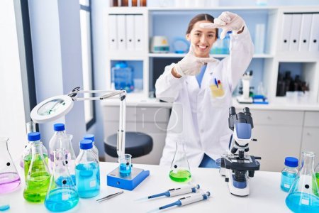 Photo for Young brunette woman working at scientist laboratory smiling making frame with hands and fingers with happy face. creativity and photography concept. - Royalty Free Image