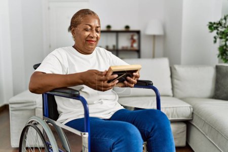 Foto de Mujer afroamericana mayor mirando foto sentada en silla de ruedas en casa - Imagen libre de derechos