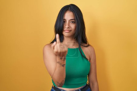 Photo for Brunette woman standing over yellow background showing middle finger, impolite and rude fuck off expression - Royalty Free Image