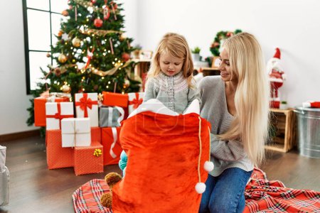 Foto de Madre e hija sosteniendo regalos en la bolsa de Navidad sentadas en el suelo en casa - Imagen libre de derechos