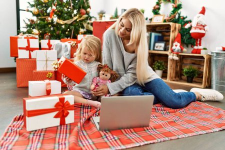 Foto de Madre e hija usando portátil sentado junto al árbol de Navidad en casa - Imagen libre de derechos