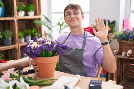Téléchargez les photos : Homme blond caucasien travaillant à la boutique de fleuristes renonçant à dire bonjour heureux et souriant, geste de bienvenue amical - en image libre de droit