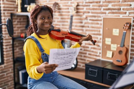 Photo for African american woman musician playing violin looking music sheet at music studio - Royalty Free Image