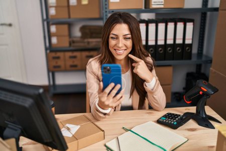 Téléchargez les photos : Jeune femme brune travaillant dans une petite entreprise ecommerce faire appel vidéo sourire heureux pointant avec la main et le doigt - en image libre de droit