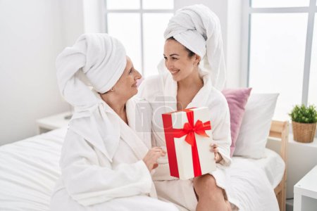 Téléchargez les photos : Mother and daughter wearing bathrobe surprise with gift at bedroom - en image libre de droit