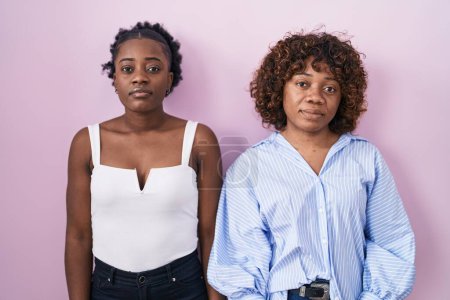 Photo for Two african women standing over pink background relaxed with serious expression on face. simple and natural looking at the camera. - Royalty Free Image