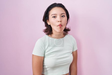 Téléchargez les photos : Hispanic young woman standing over pink background making fish face with lips, crazy and comical gesture. funny expression. - en image libre de droit
