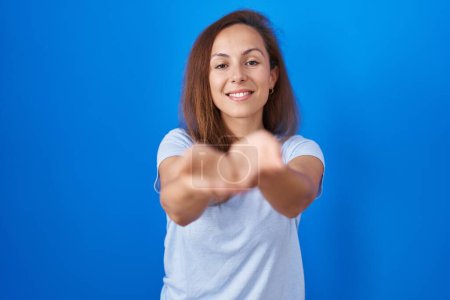 Téléchargez les photos : Brunette femme debout sur fond bleu souriant avec les mains paumes ensemble recevant ou donnant geste. maintien et protection - en image libre de droit