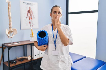 Photo for Young physiotherapist woman holding foam roll at the clinic covering mouth with hand, shocked and afraid for mistake. surprised expression - Royalty Free Image