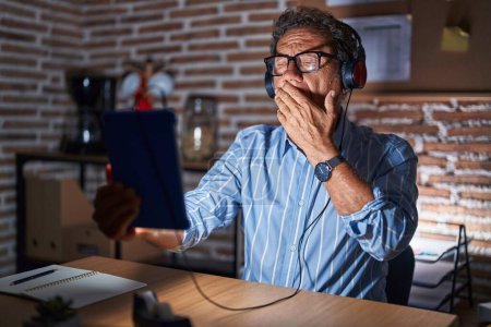 Foto de Middle age hispanic man using touchpad sitting on the table at night bored yawning tired covering mouth with hand. restless and sleepiness. - Imagen libre de derechos