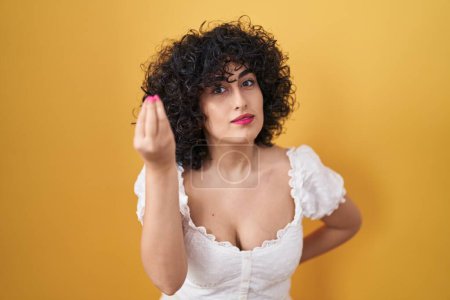 Téléchargez les photos : Jeune femme brune avec les cheveux bouclés debout sur fond jaune faisant geste italien avec la main et les doigts expression confiante - en image libre de droit