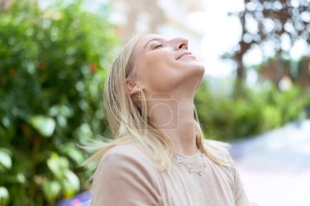 Foto de Mujer rubia joven respirando con los ojos cerrados en el parque - Imagen libre de derechos