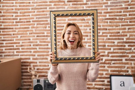 Photo for Hispanic woman holding empty frame smiling and laughing hard out loud because funny crazy joke. - Royalty Free Image