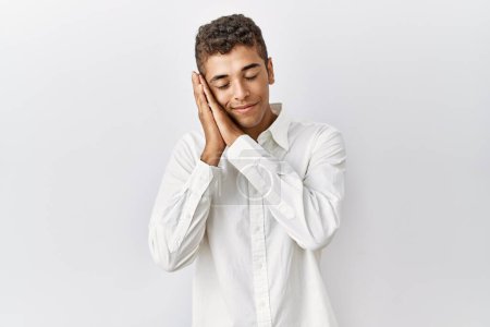 Photo for Young handsome hispanic man standing over isolated background sleeping tired dreaming and posing with hands together while smiling with closed eyes. - Royalty Free Image