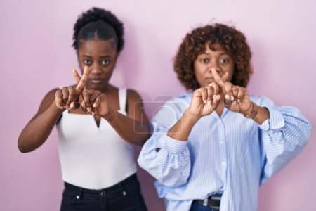 Téléchargez les photos : Deux femmes africaines debout sur fond rose expression de rejet croisant les doigts faisant signe négatif - en image libre de droit