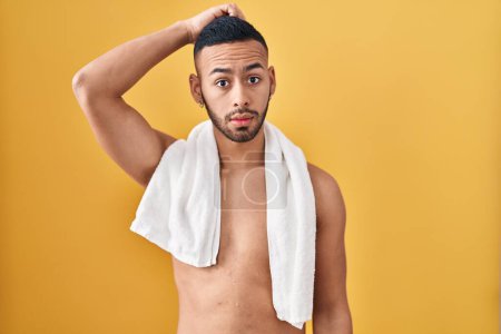 Photo for Young hispanic man standing shirtless with towel confuse and wondering about question. uncertain with doubt, thinking with hand on head. pensive concept. - Royalty Free Image